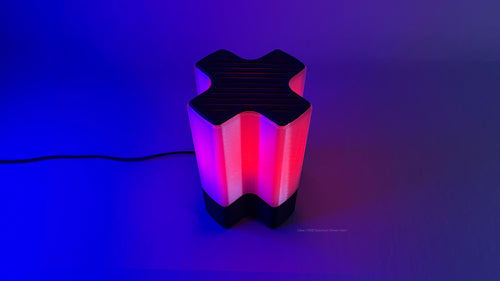 Front angled view of Nebu 3D printed modern tabletop lamp in clear shade, showing double-walled transparent design with lamp on in RGB mode