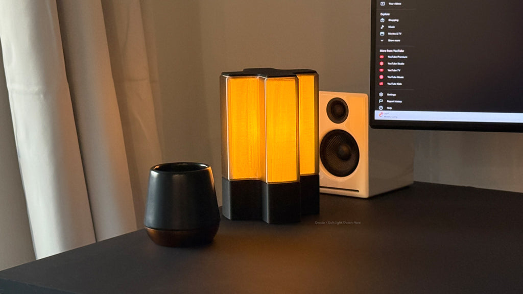 Front three-quarter view of Nebu 3D printed modern tabletop lamp in smoke shade, shown on with soft ambient light