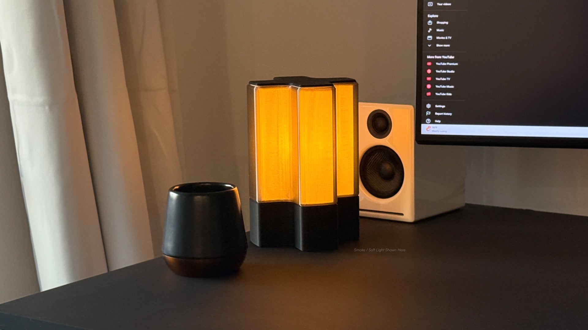 Front three-quarter view of Nebu 3D printed modern tabletop lamp in smoke shade, shown on with soft ambient light
